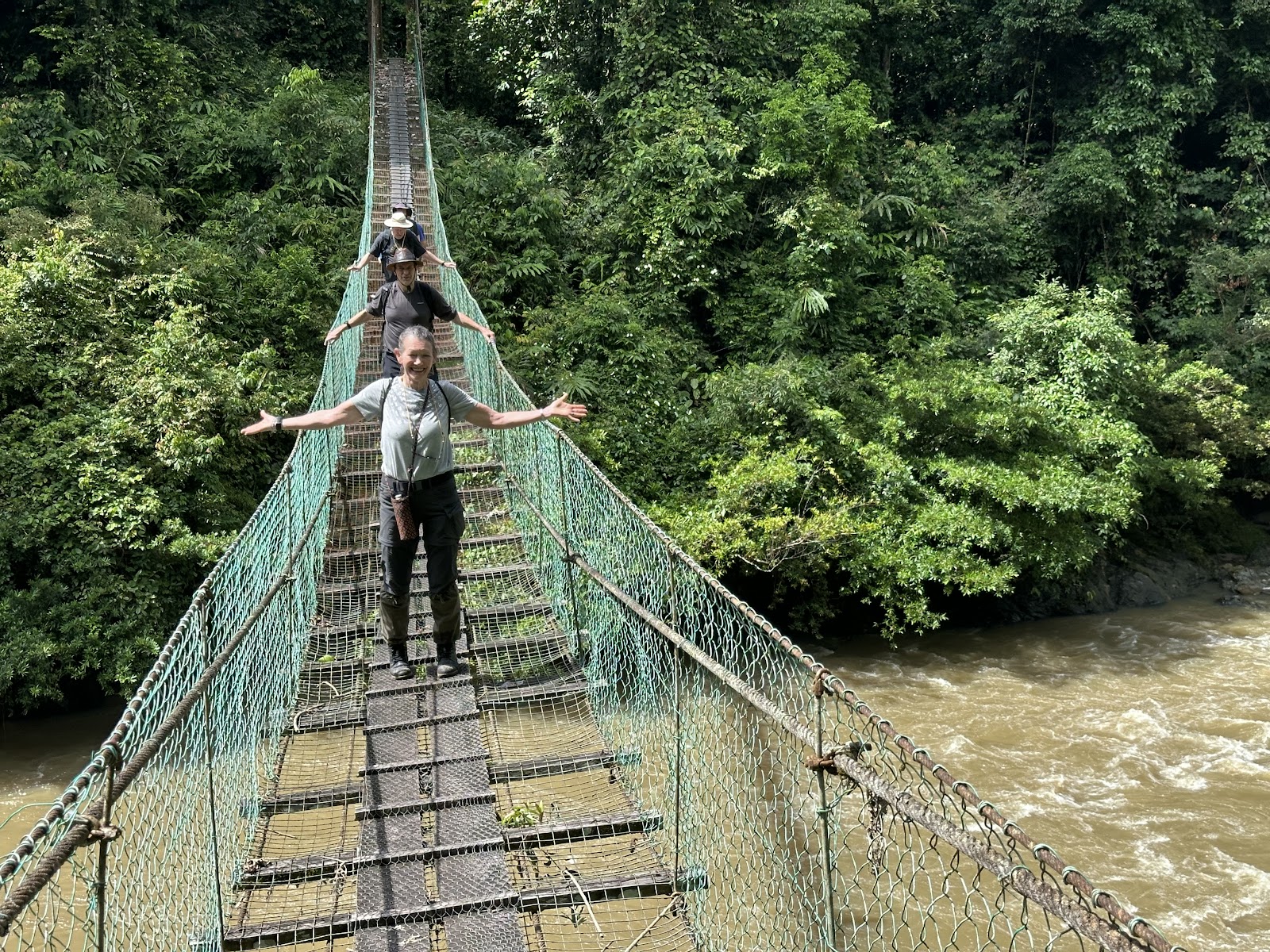 Two men crossing a rope suspension bridge over a jungle river