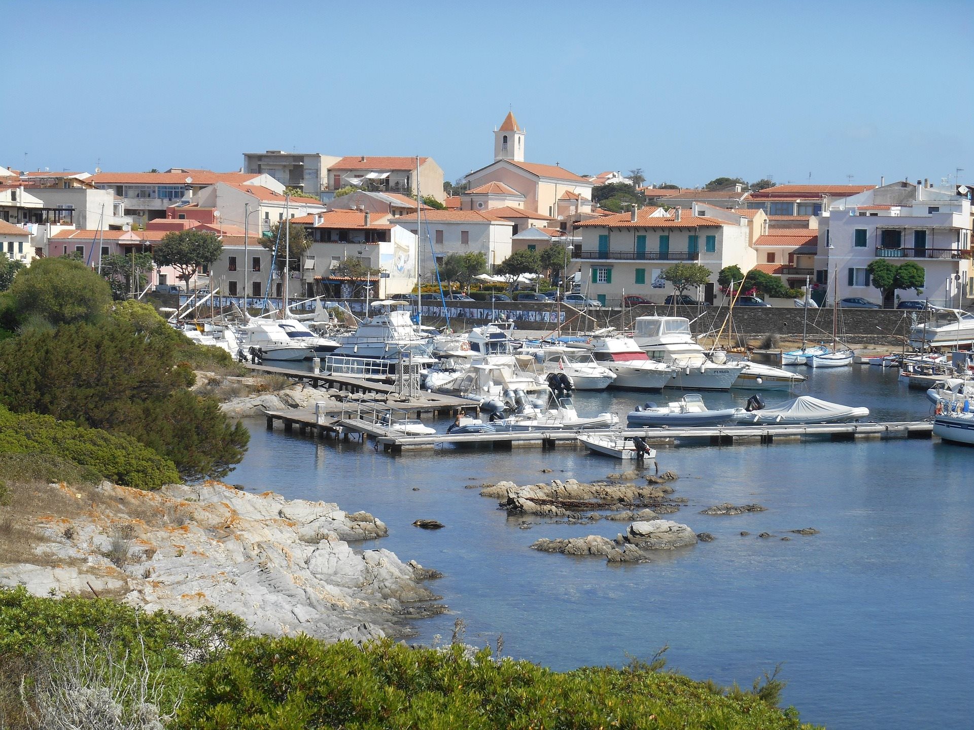 Boats moored in a marina beneath a Sardinian coastal town