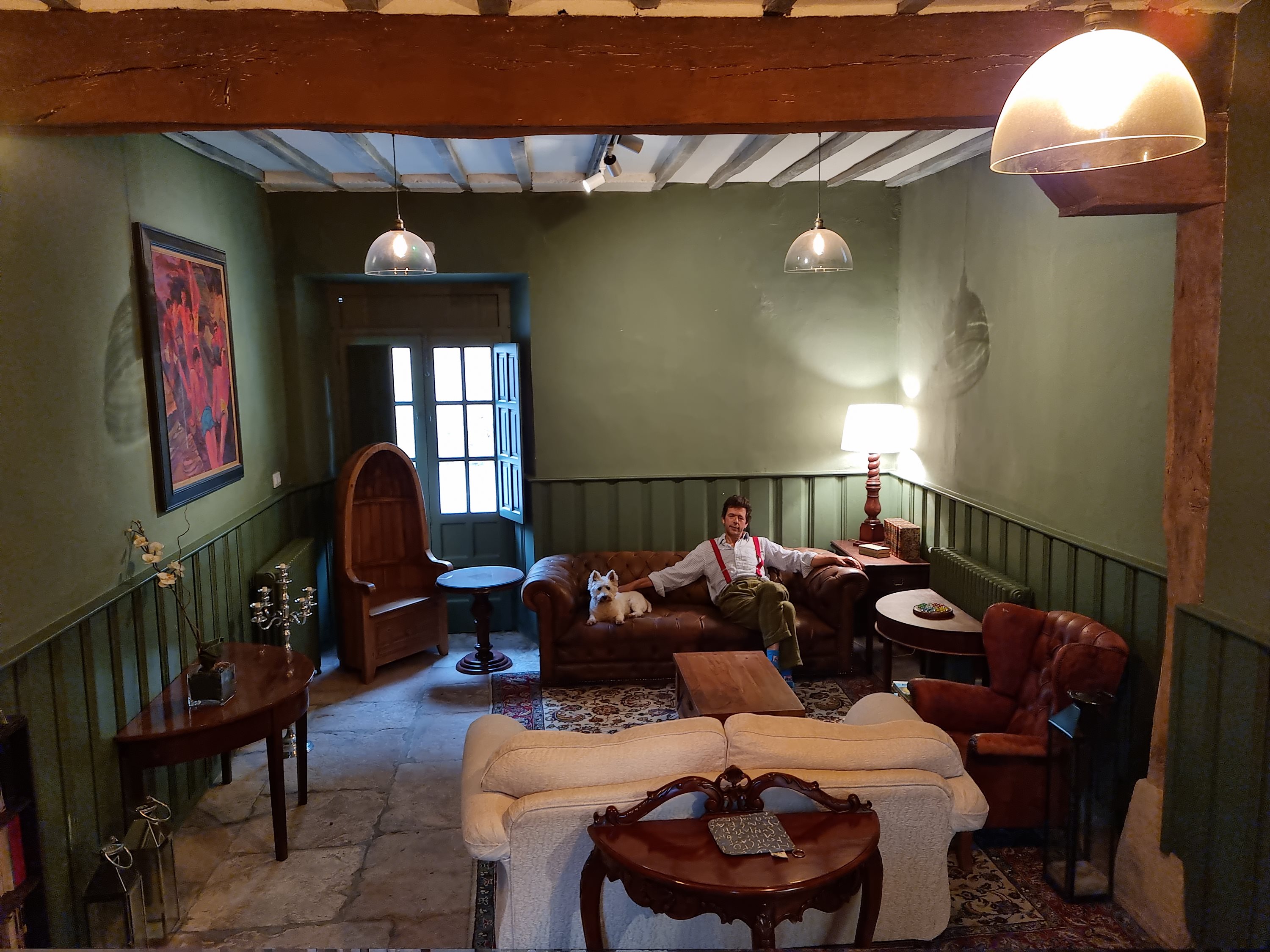 A cosy green panelled lounge with leather furniture, a man sitting with his dog