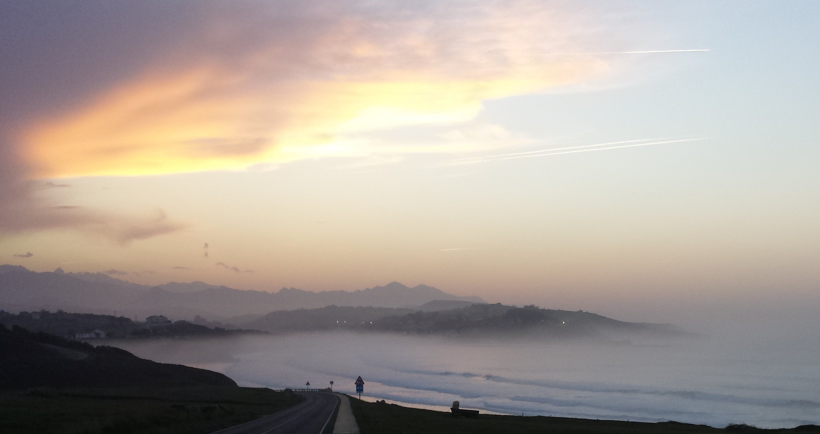 Misty coastal sunset over cliffs and a winding road