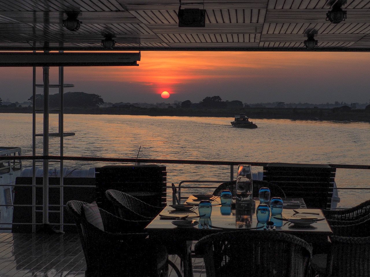 A dining table set on a boat deck overlooking the river at sunset