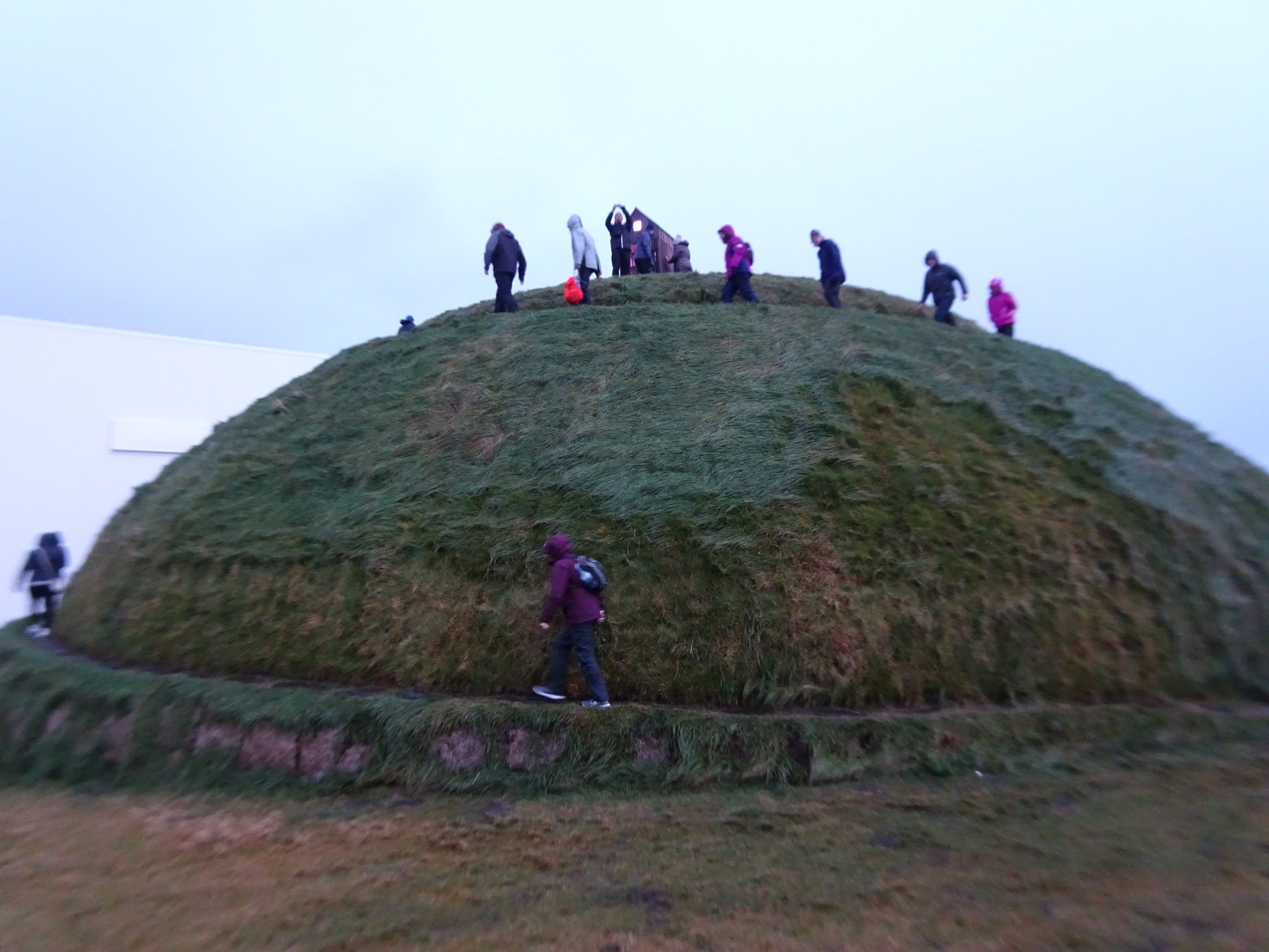 Visitors climbing a large grass-covered mound in Iceland