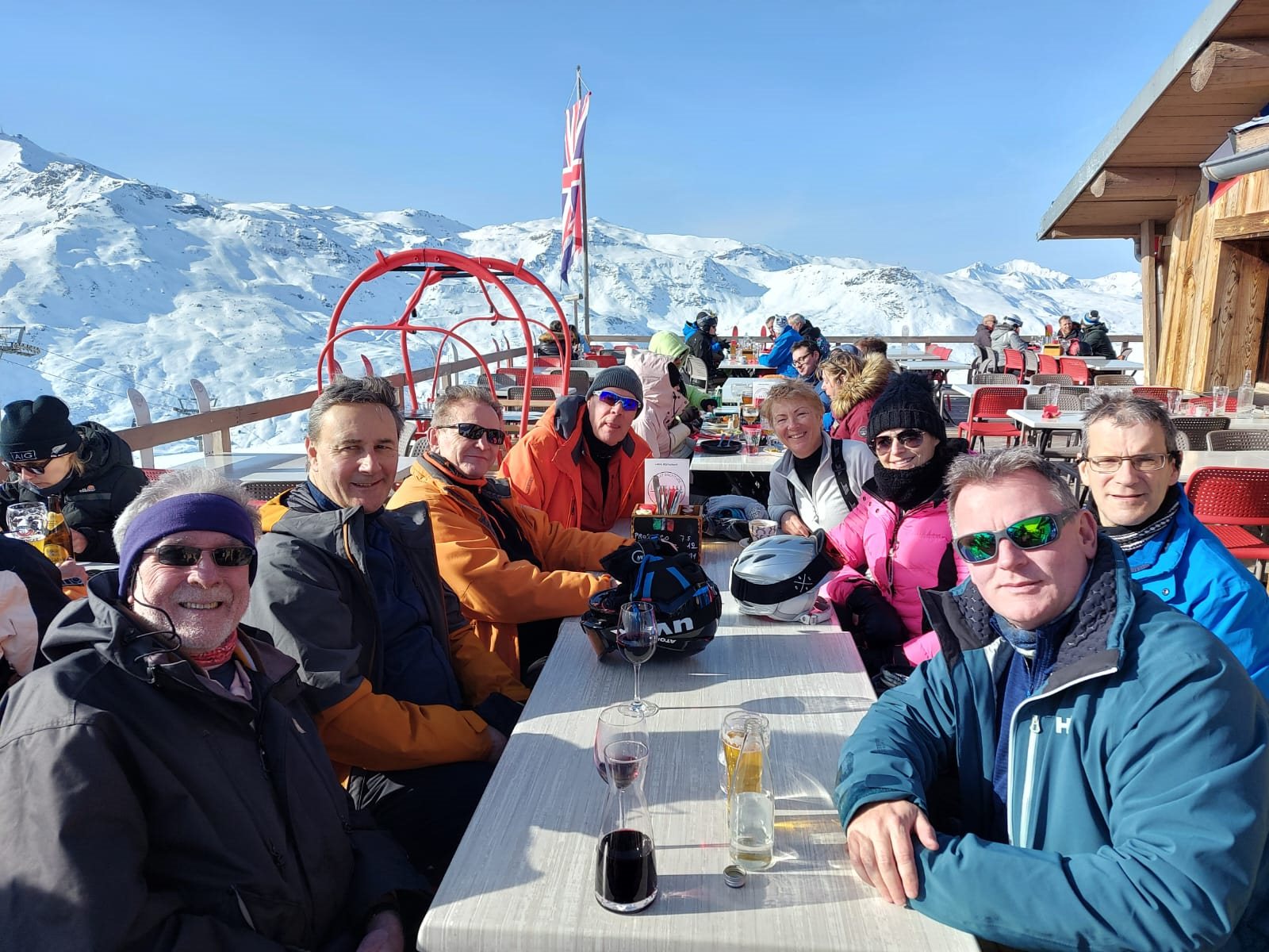 A group of skiers posing with drinks at a mountain restaurant terrace