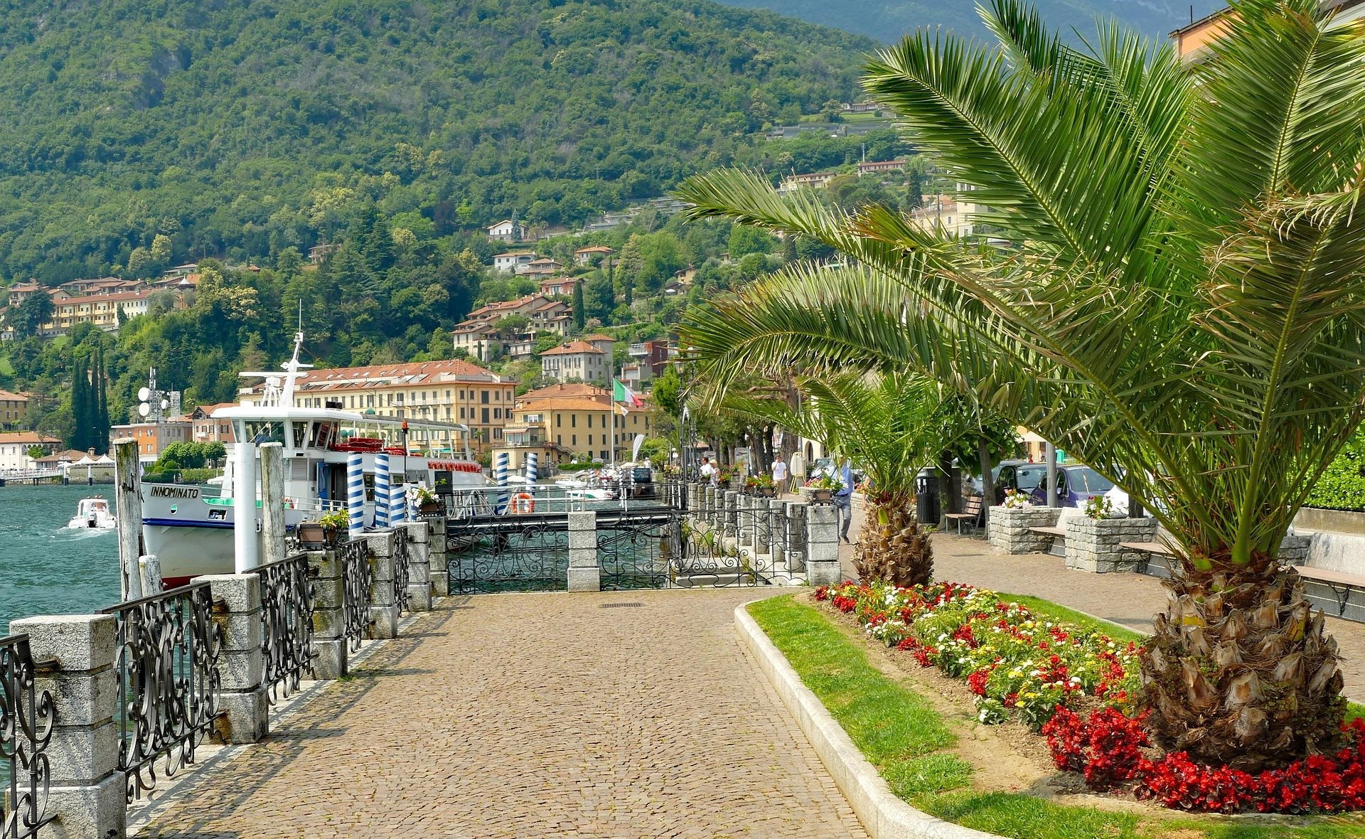 Lakeside promenade with palm trees and a passenger boat moored beyond