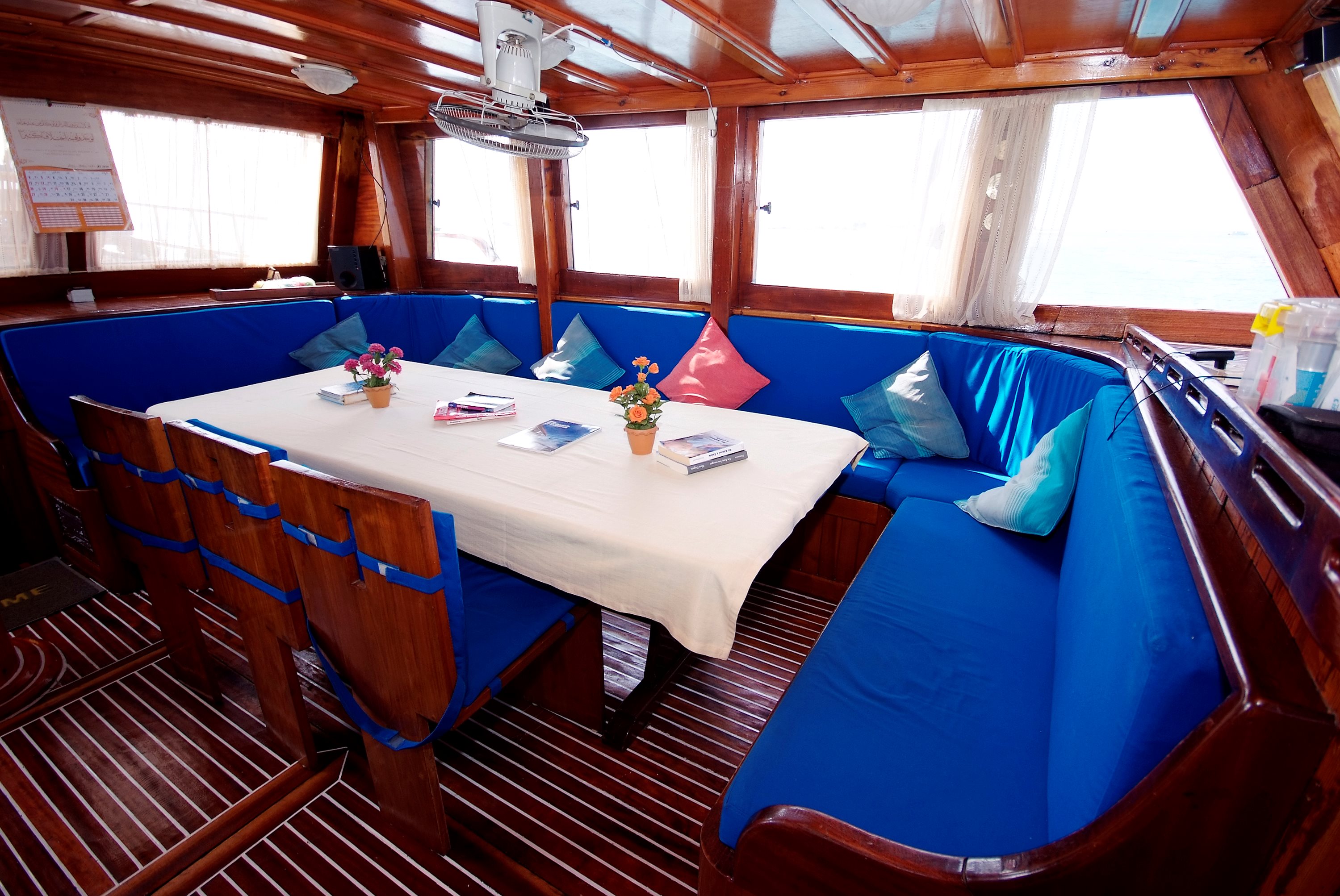 Wood-panelled saloon on a boat with a dining table and blue cushioned seating