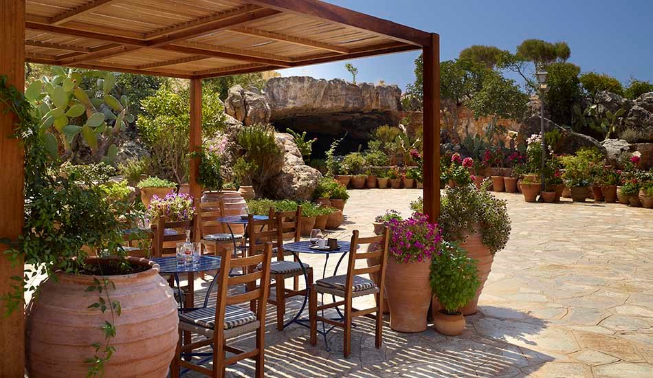 A shaded taverna terrace with wooden pergola and potted plants