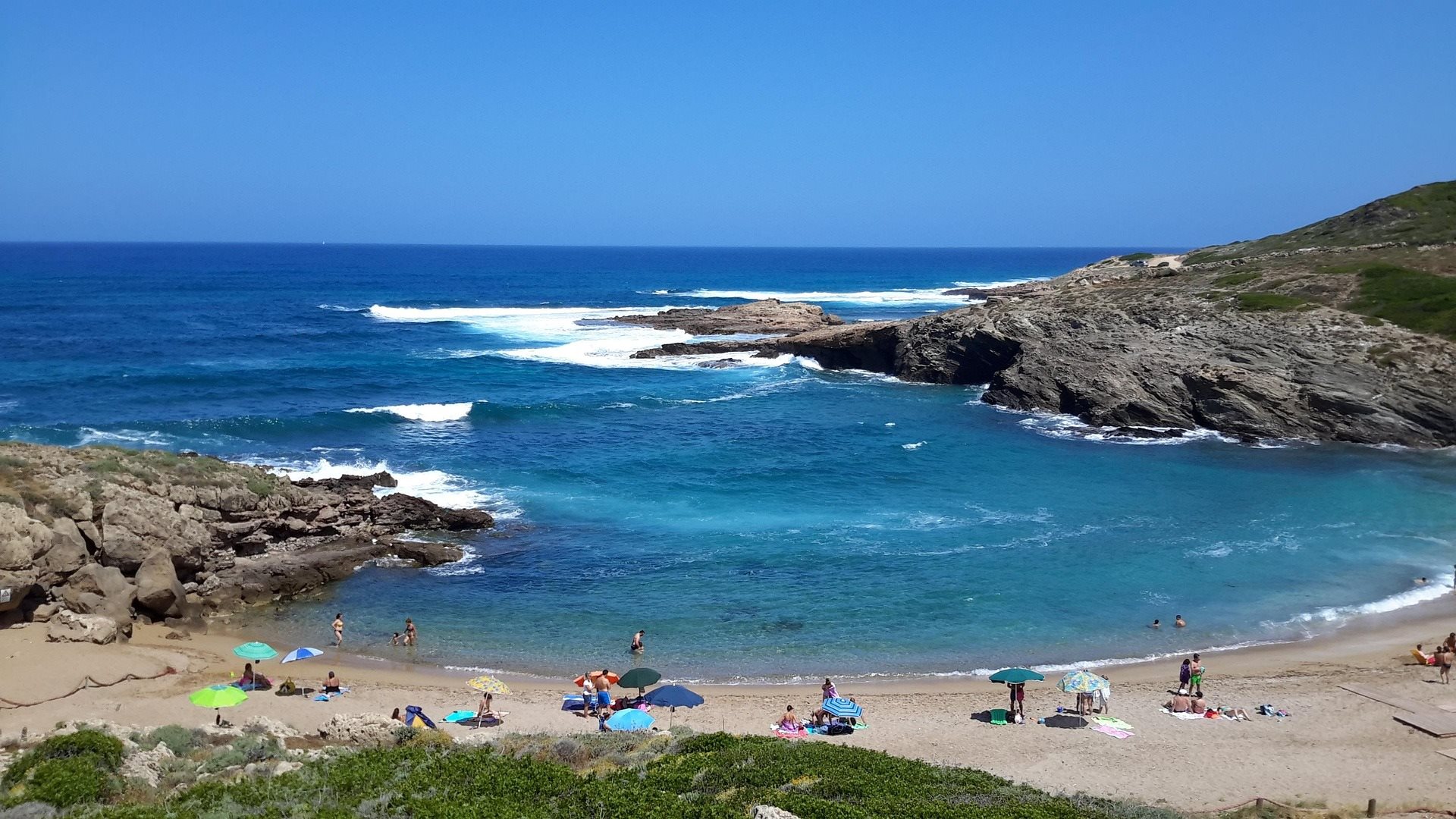 A rocky cove beach with swimmers and sunbathers in the turquoise water