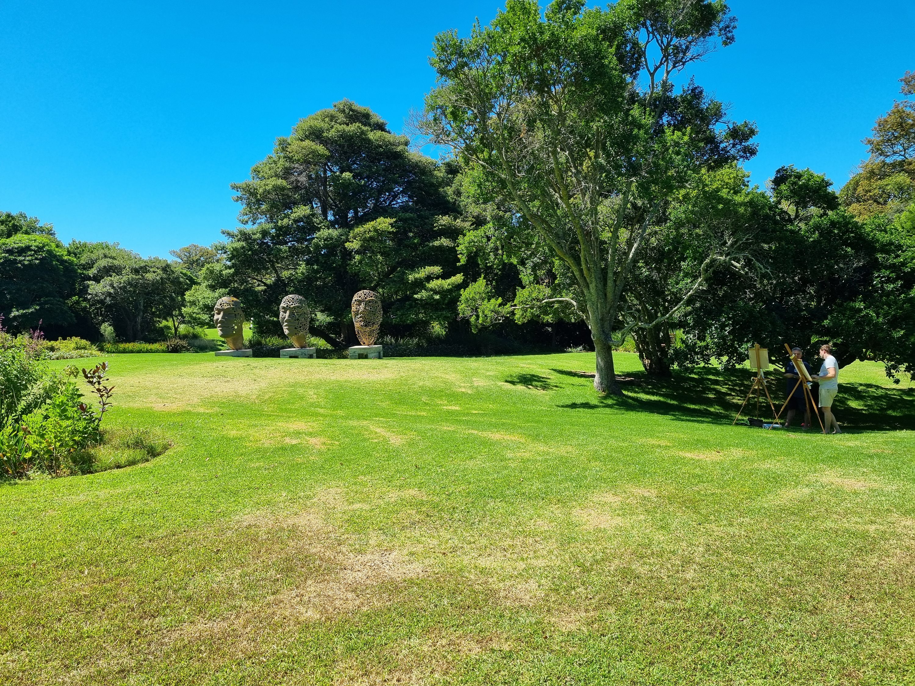 Large stone head sculptures on a lawn in a botanical garden
