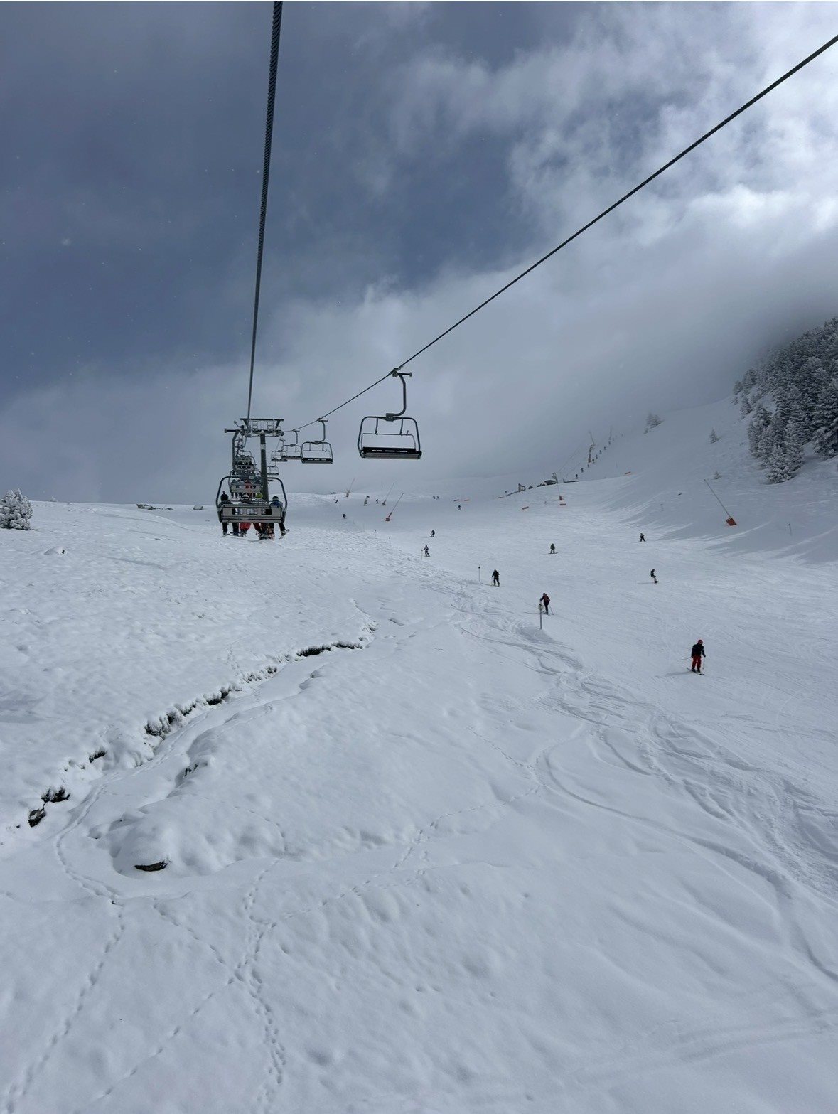 Chairlift above a snowy ski slope with skiers in the distance