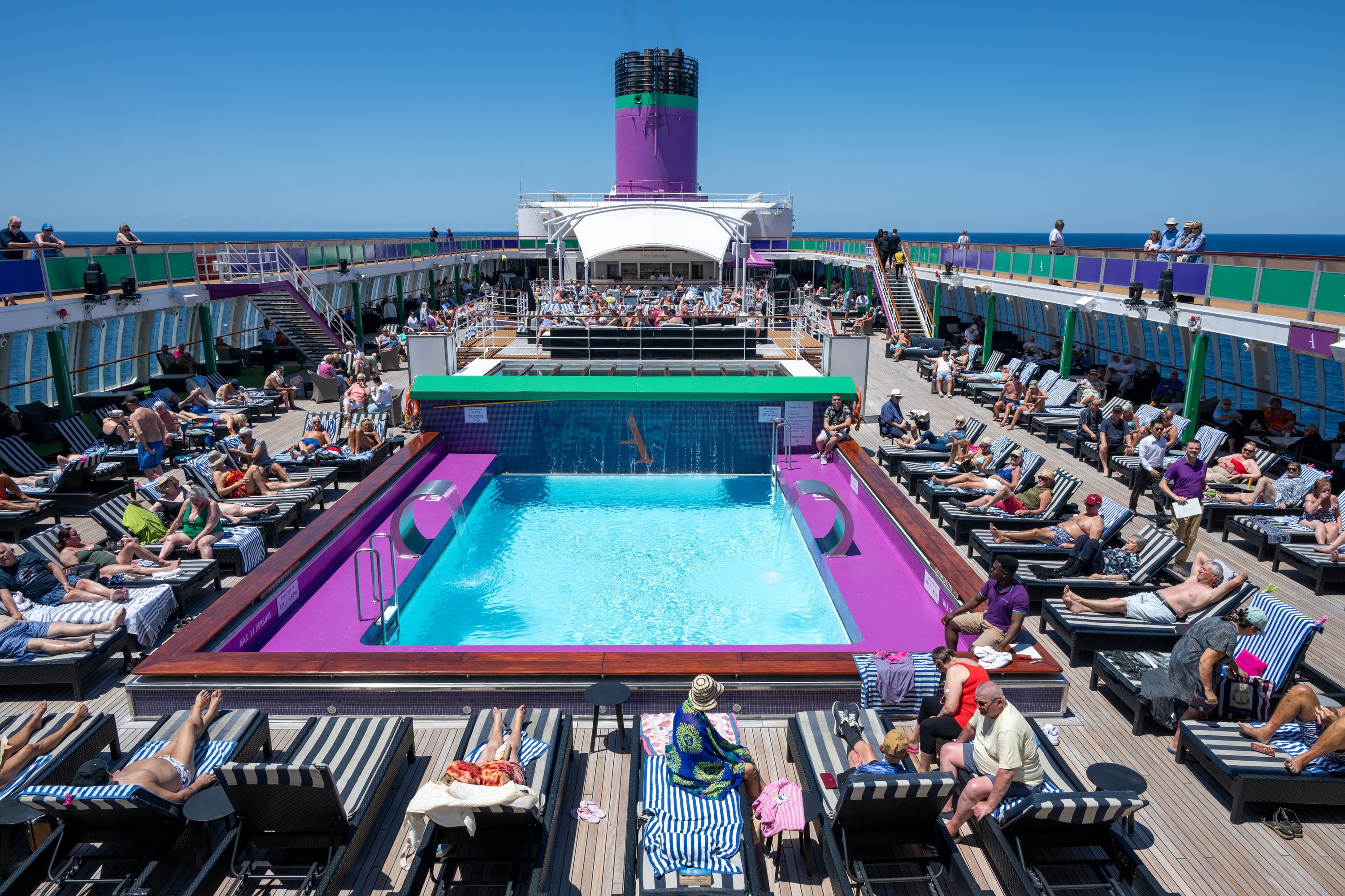 Sun loungers around a pool deck full of passengers on a cruise ship