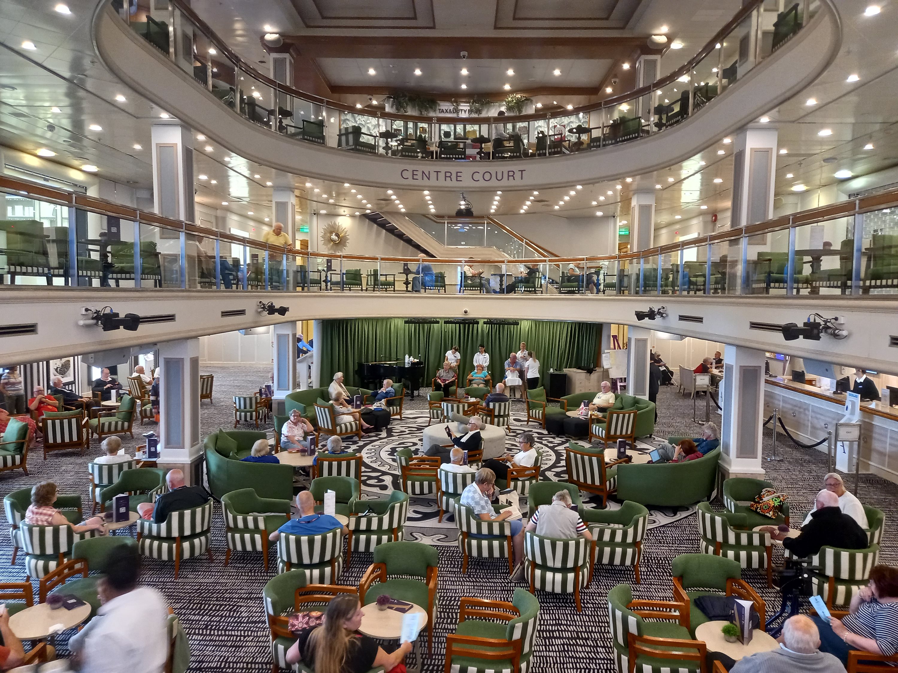 Passengers seated and chatting across a grand two-level ship atrium lounge
