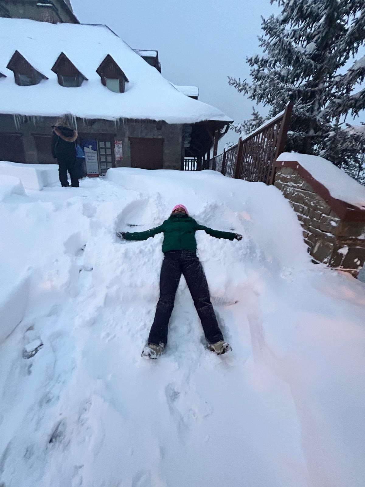 A skier making a snow angel outside a snow-covered mountain lodge