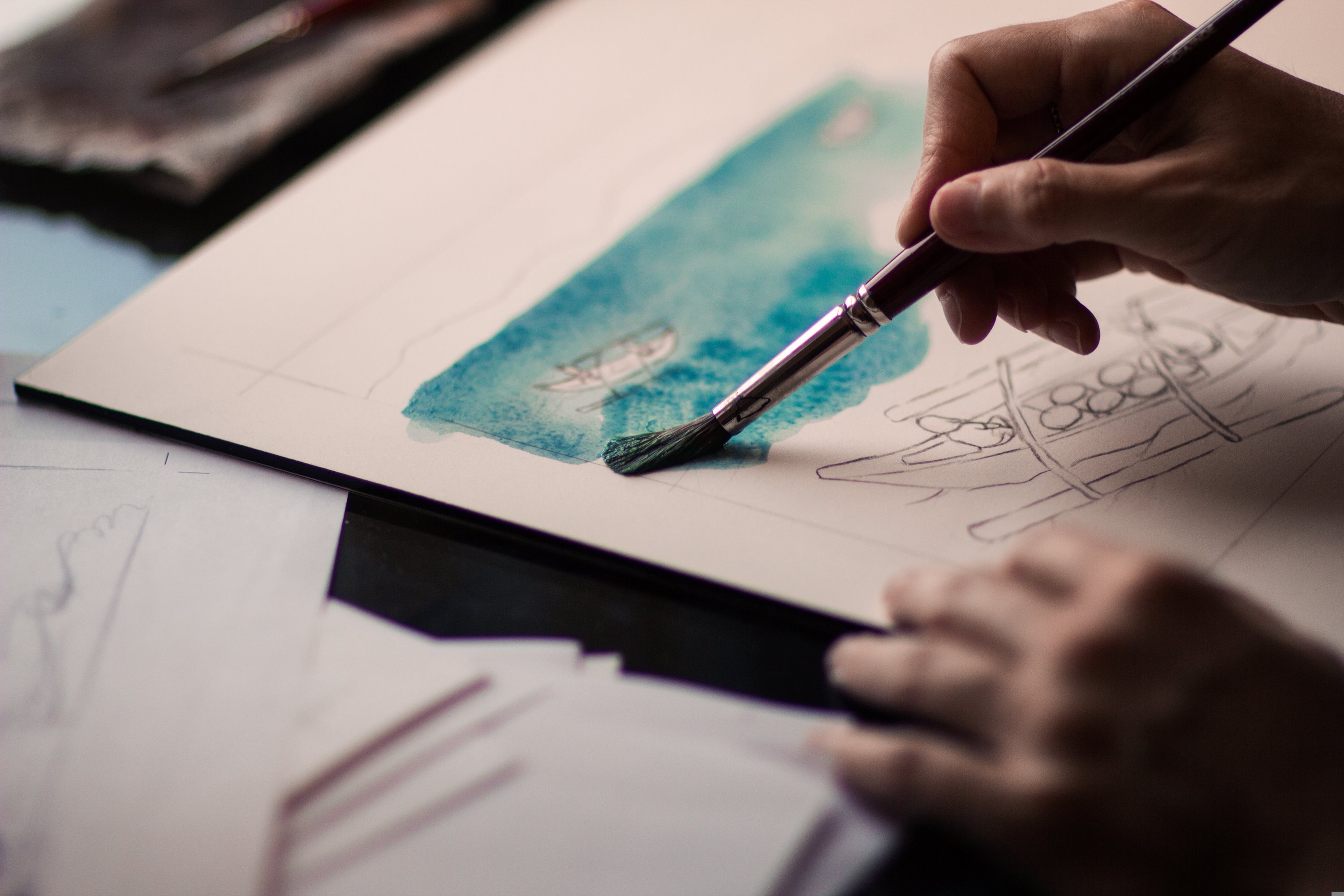 Close-up of a hand painting a blue watercolour wash onto paper