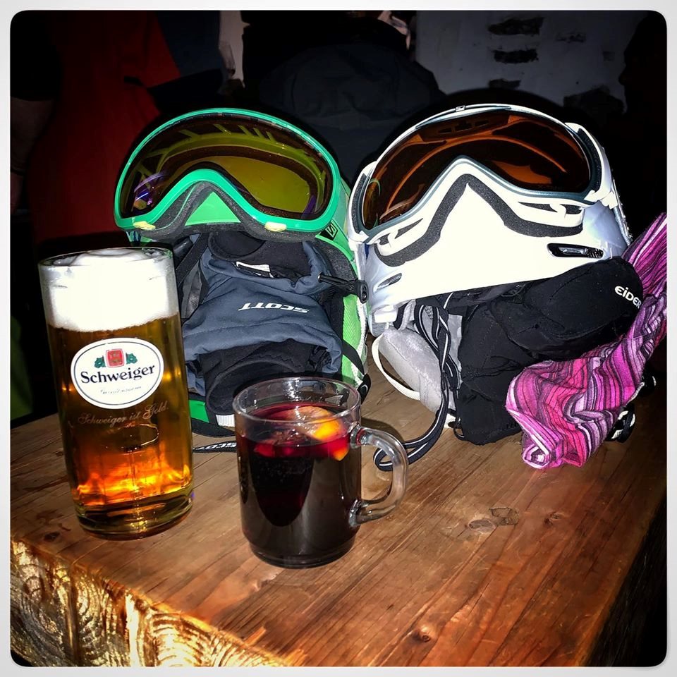 Ski helmets, goggles and gloves beside a beer and a mulled wine on a wooden table