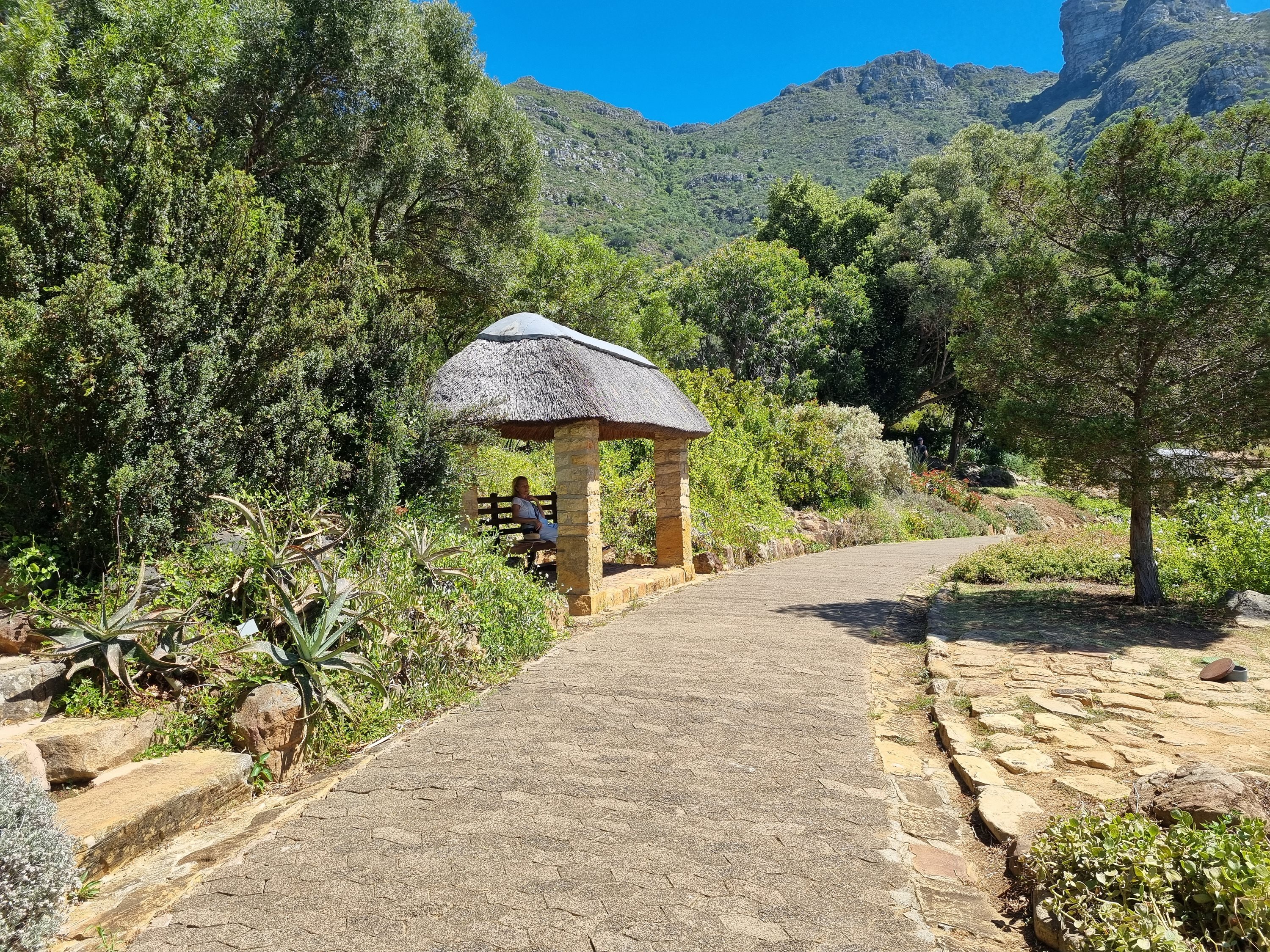 Thatched garden shelter along a paved path with mountains beyond