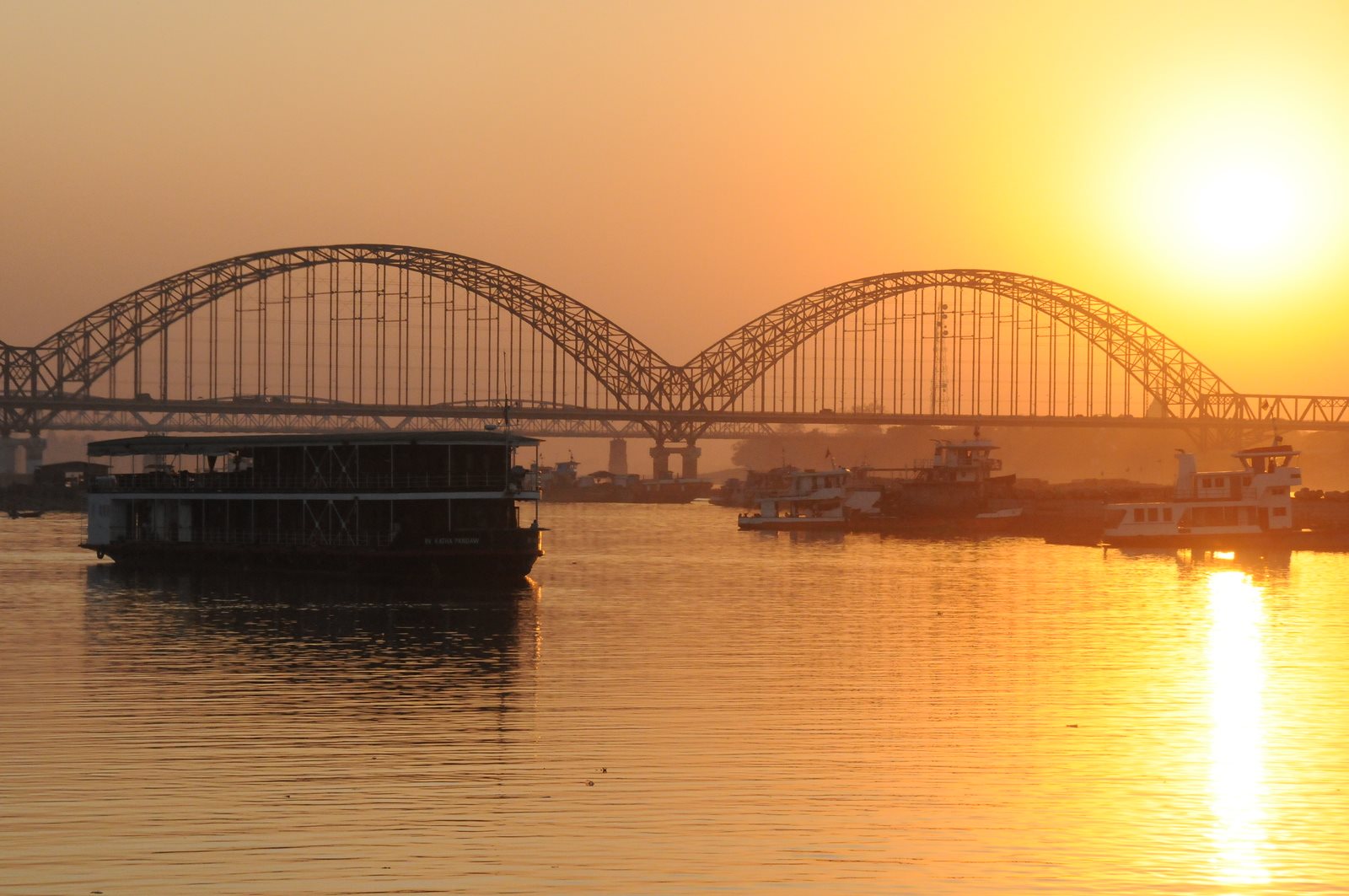 Boats on the river silhouetted against an arched bridge at sunset
