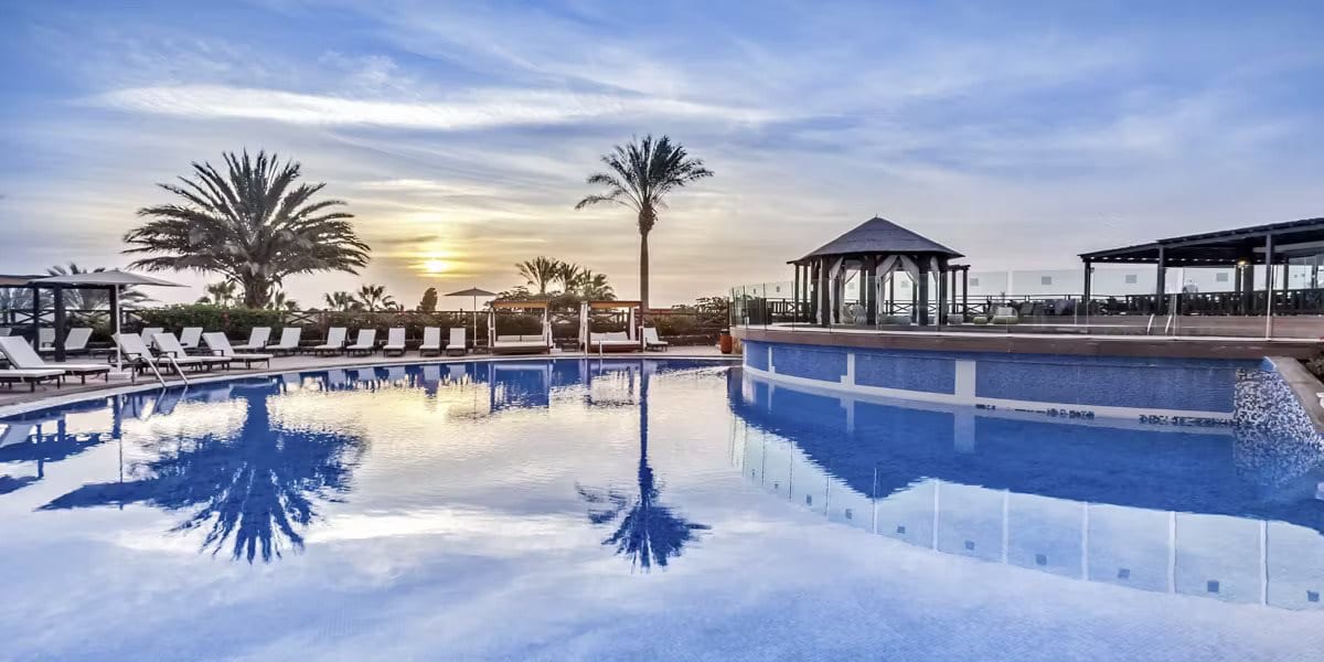 Empty resort swimming pool with palm trees at sunset