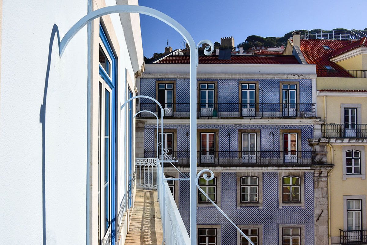 Ornate lamp brackets on a balcony overlooking a tiled apartment building