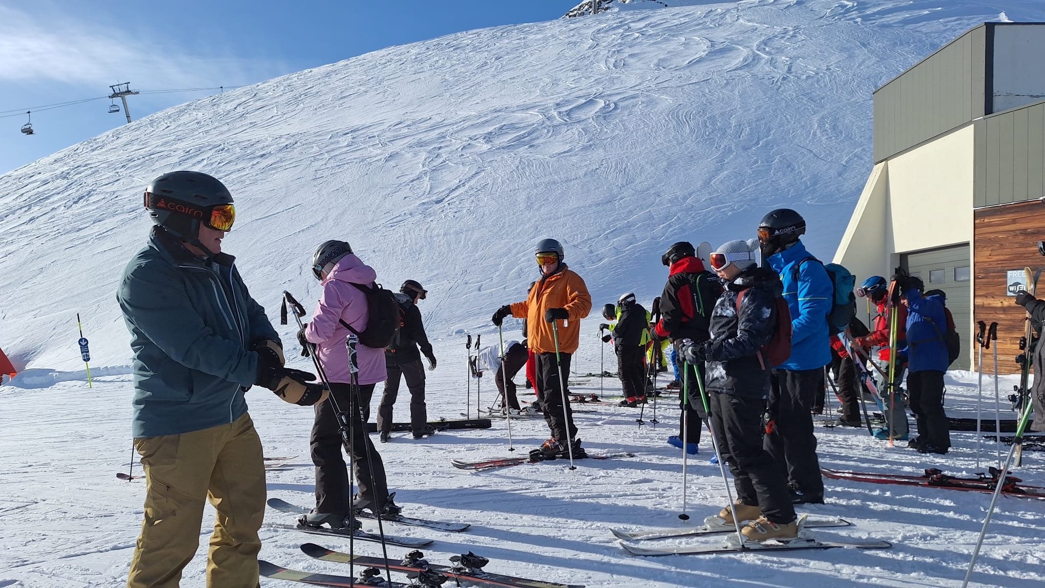 A group of skiers gathered together at the top of a run, skis on