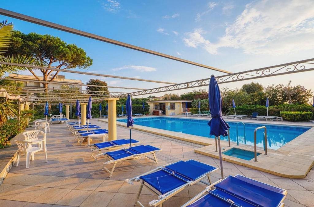 Empty poolside terrace with sun loungers and pine trees at dusk