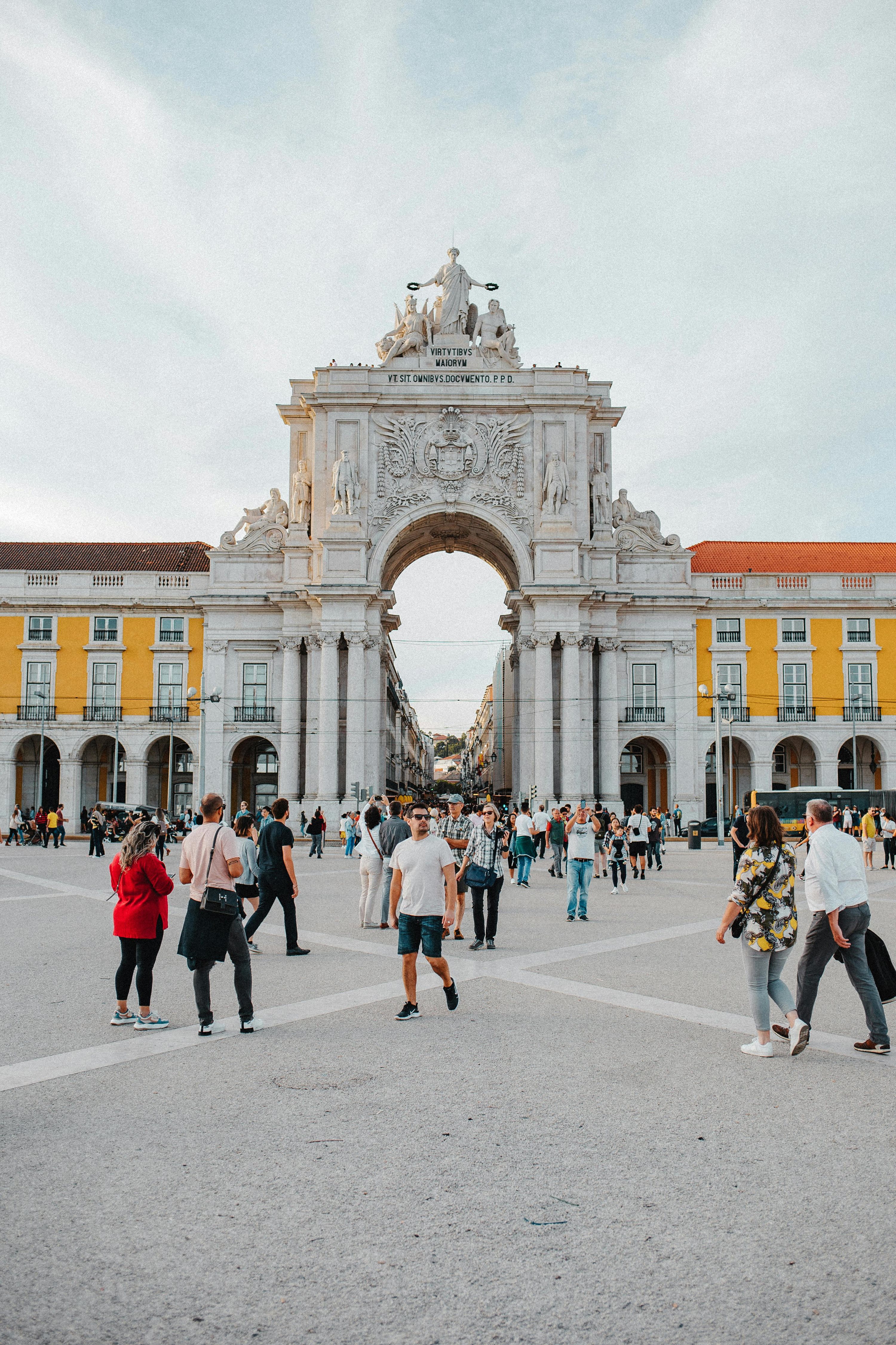 Pedestrians crossing a large square beneath a triumphal stone arch