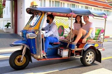 Two travellers riding in a tuk-tuk driven by a local driver