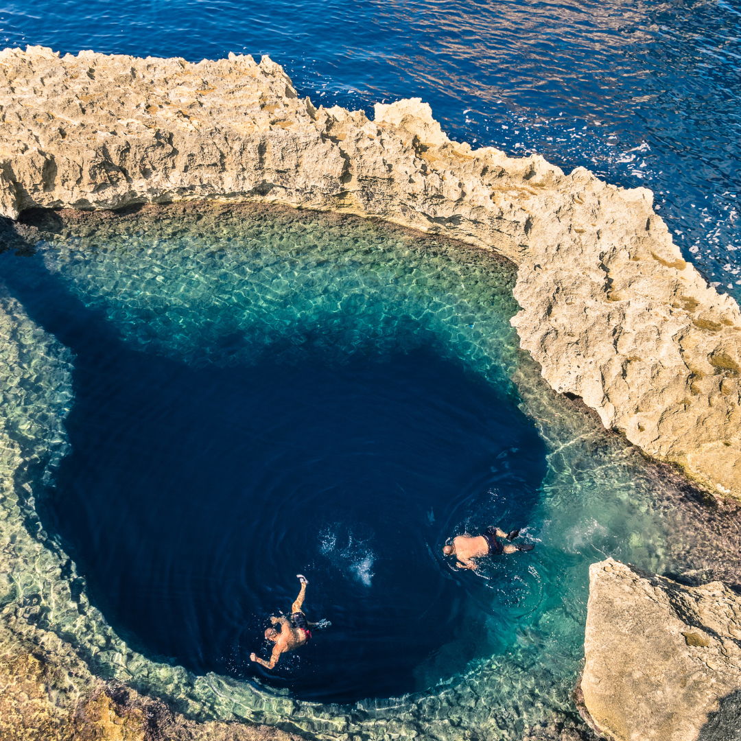 Two swimmers in a natural rock swimming hole above the sea