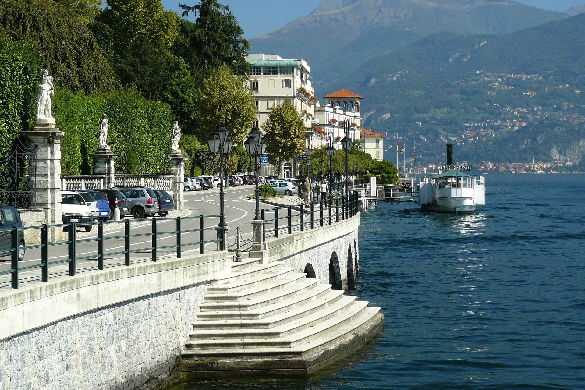 Lakeside promenade with parked cars and a passenger ferry approaching