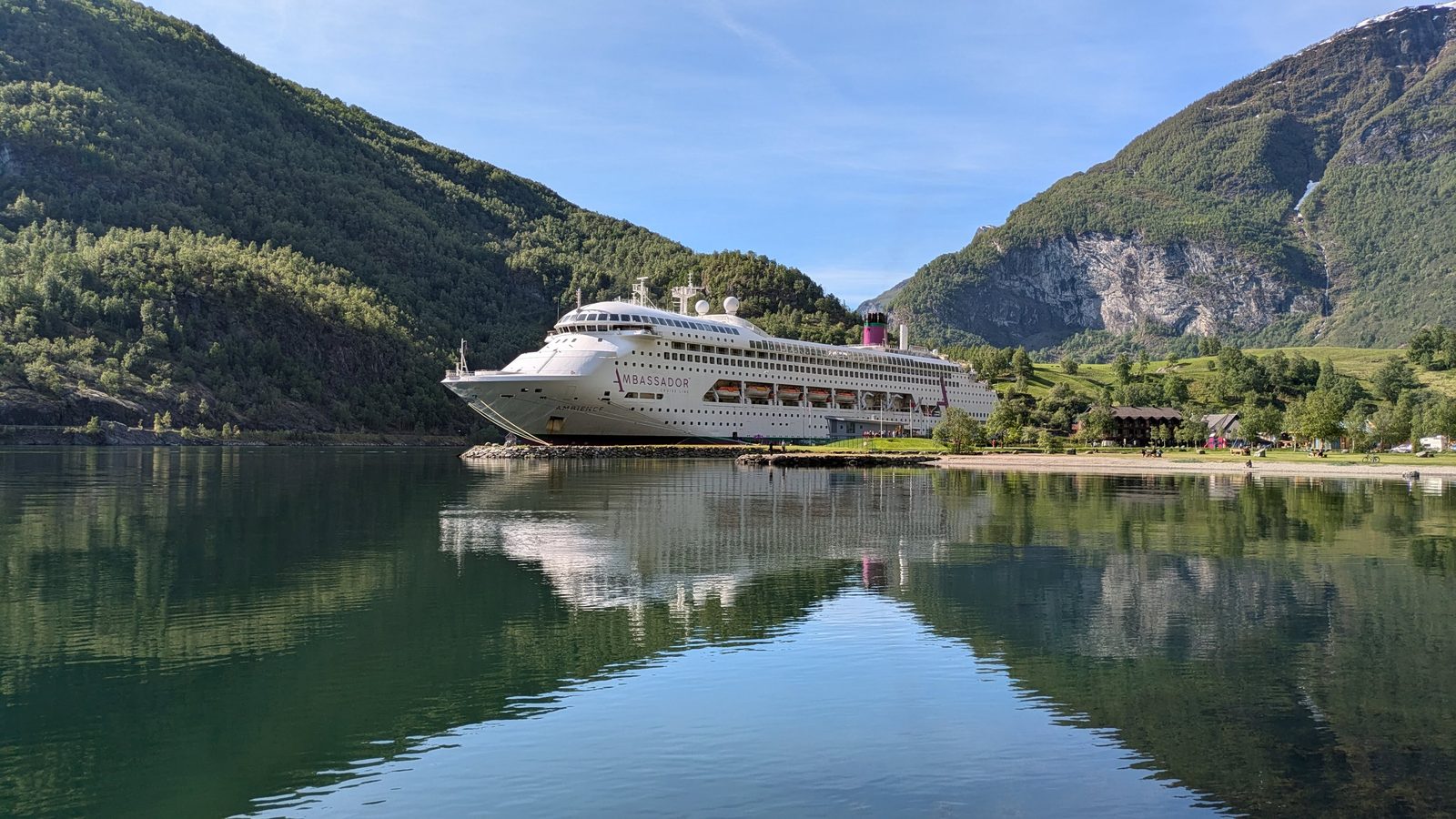 Cruise ship moored on a still fjord surrounded by green mountains