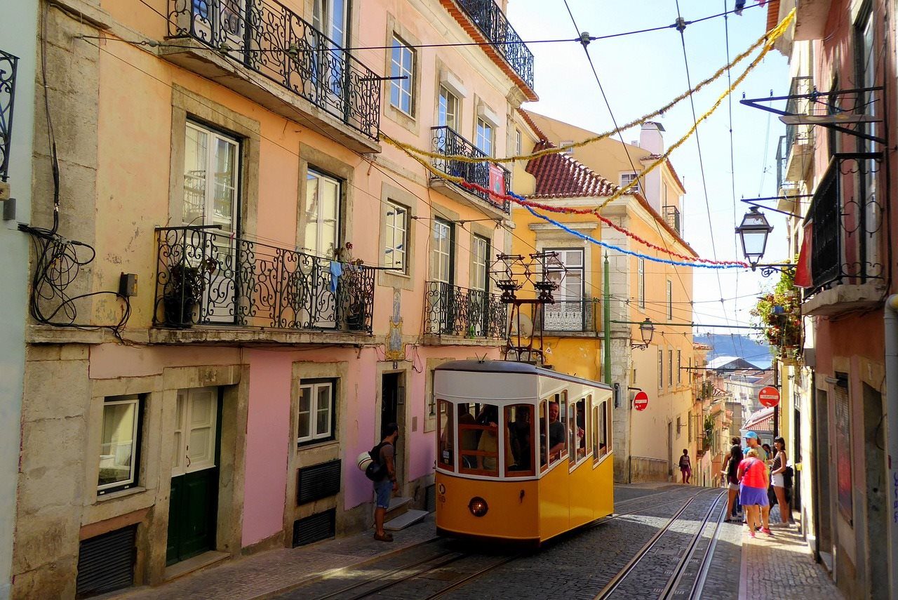 Yellow tram descending a narrow street lined with pastel-coloured buildings