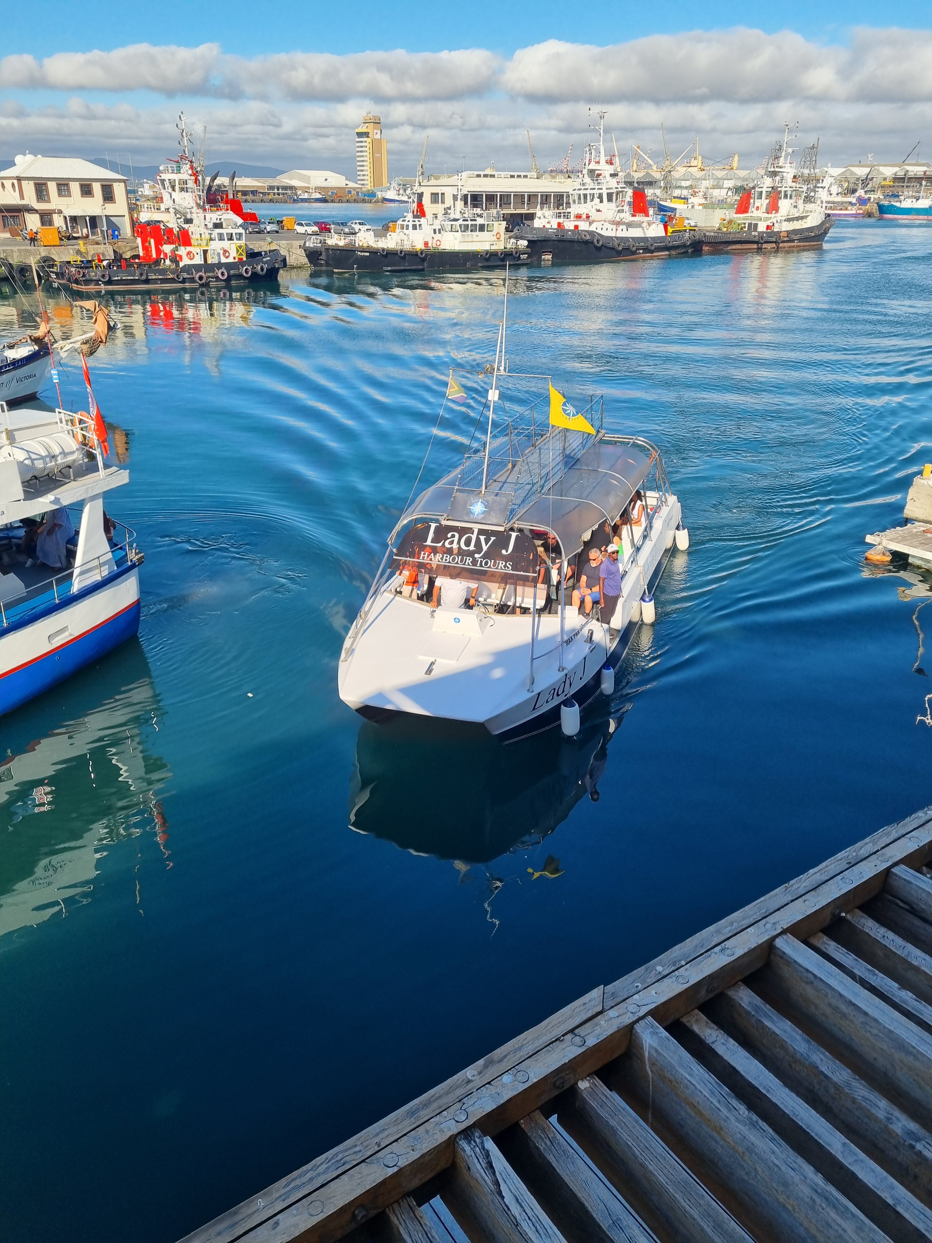 A harbour tour boat with passengers crossing Cape Town's working harbour