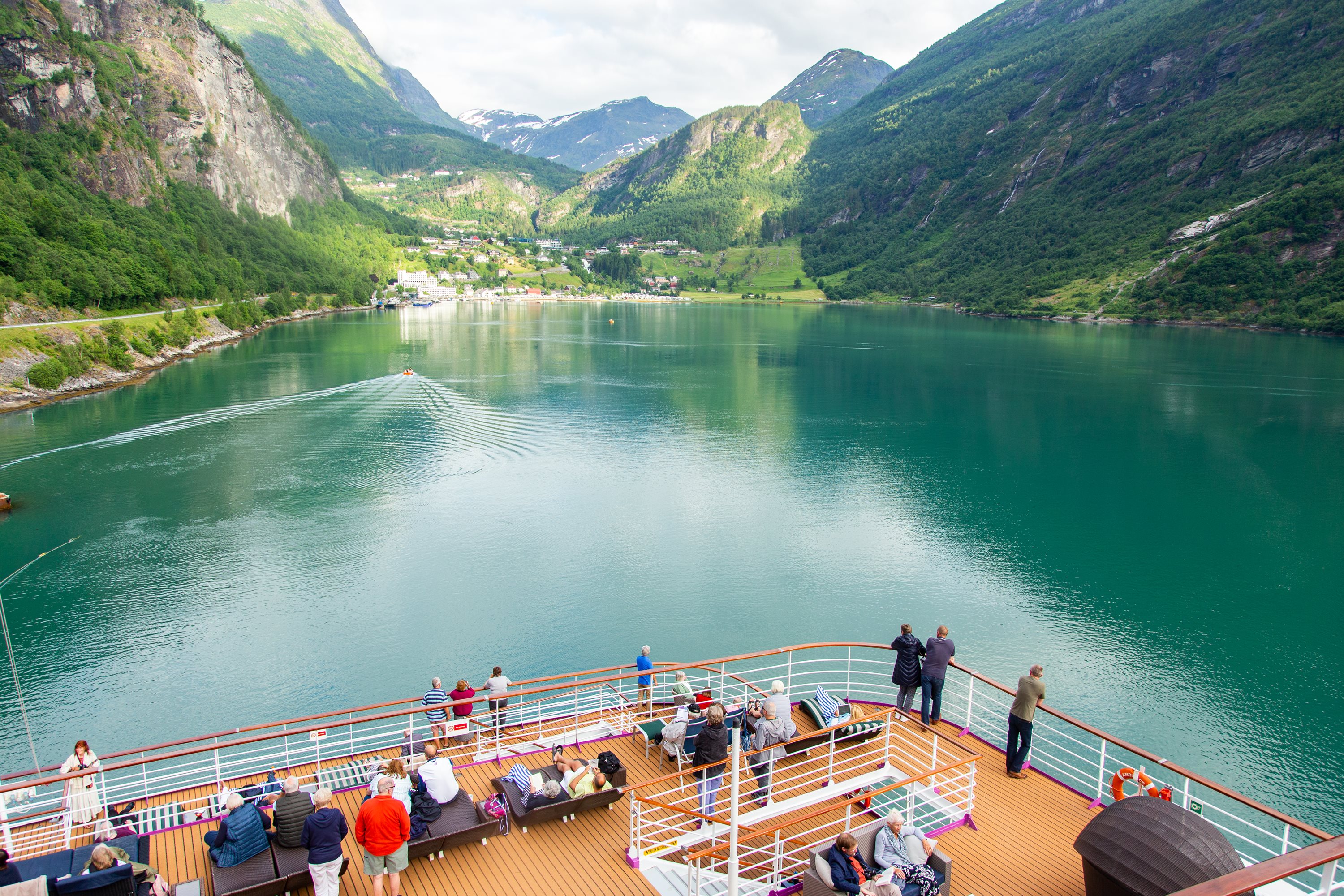 Passengers gathered on the bow of a cruise ship viewing a green fjord and mountains