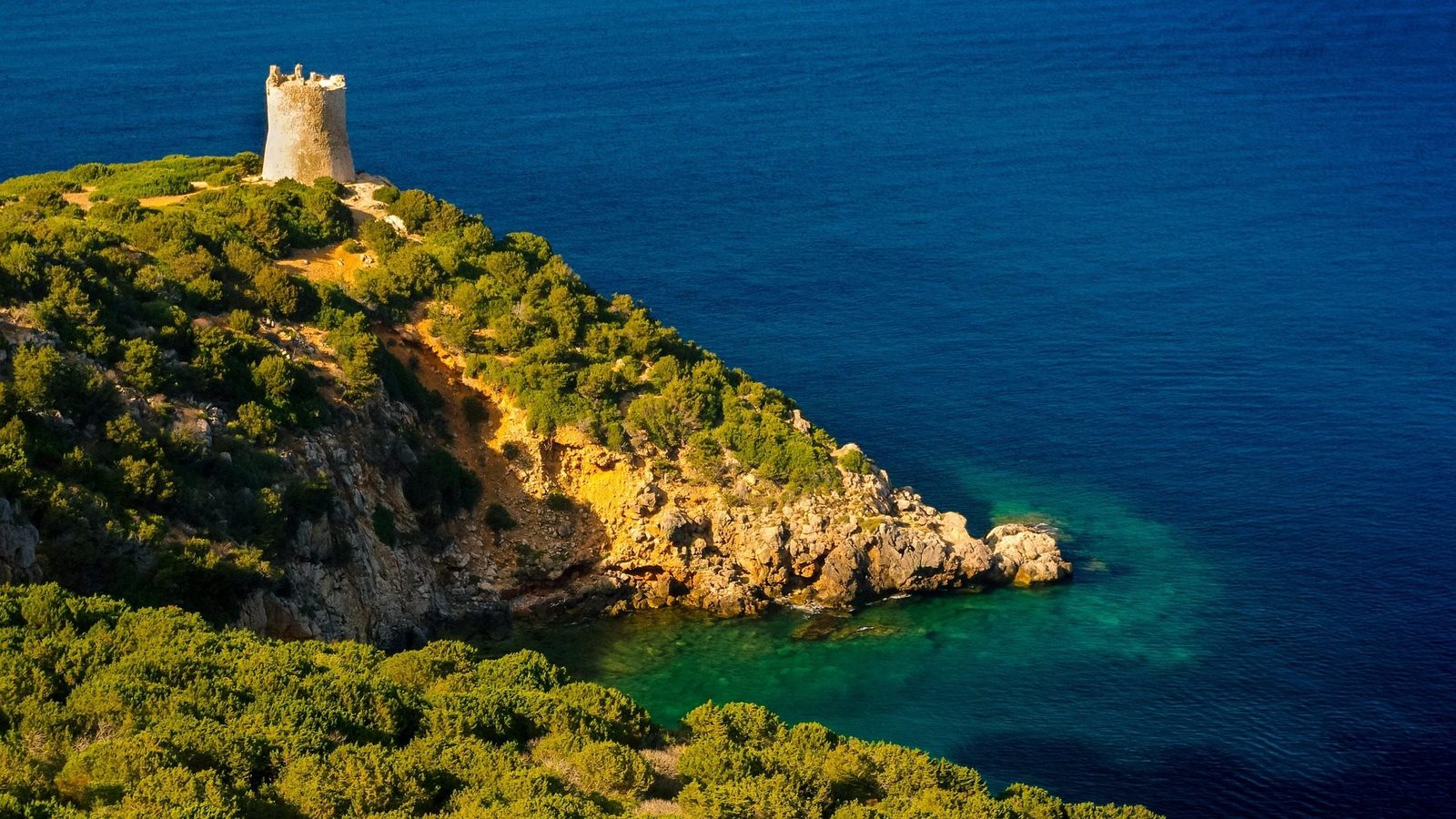 A stone coastal watchtower on a headland above a turquoise cove