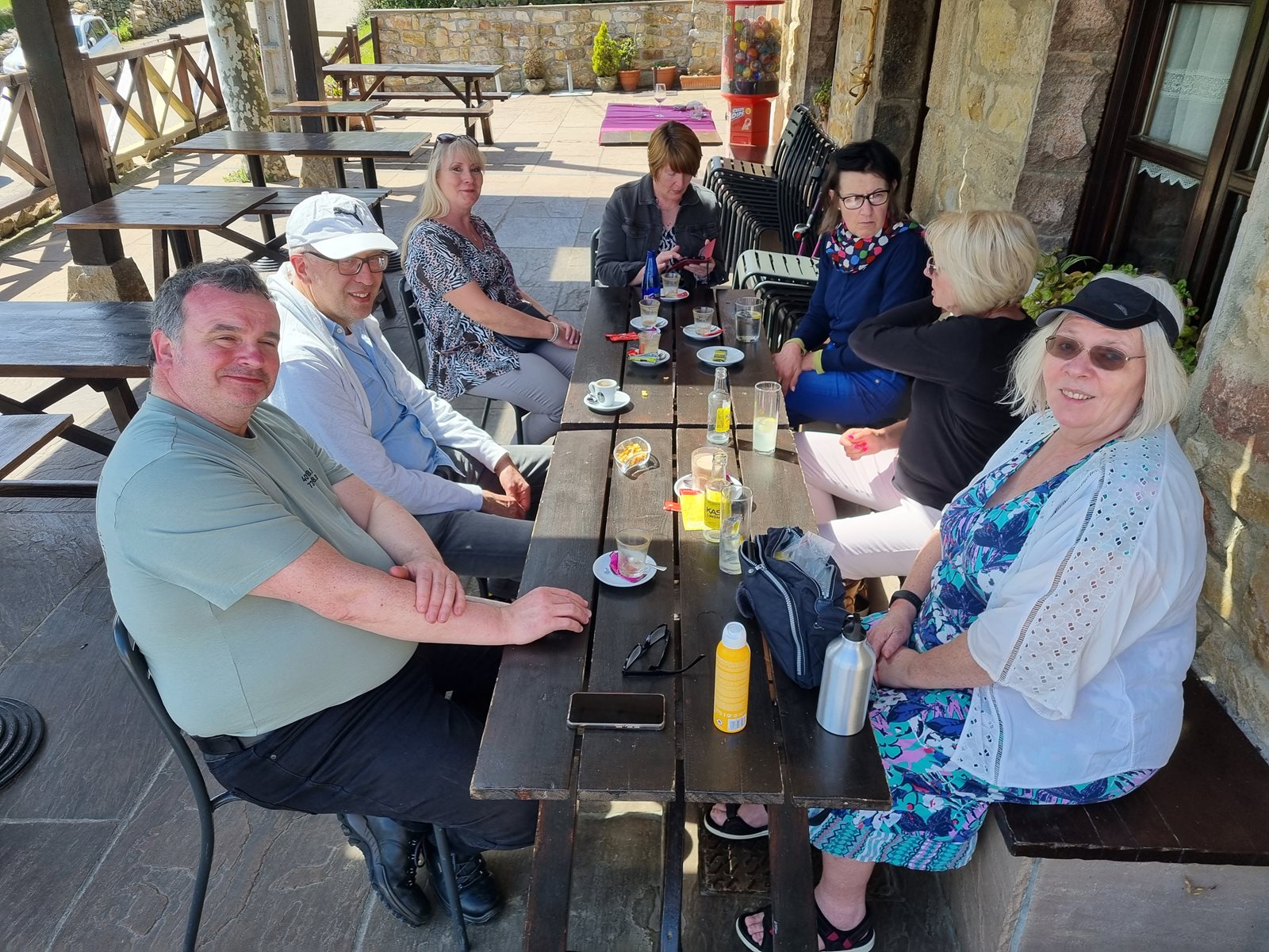 Seven travellers sitting together at an outdoor café table, smiling for the camera