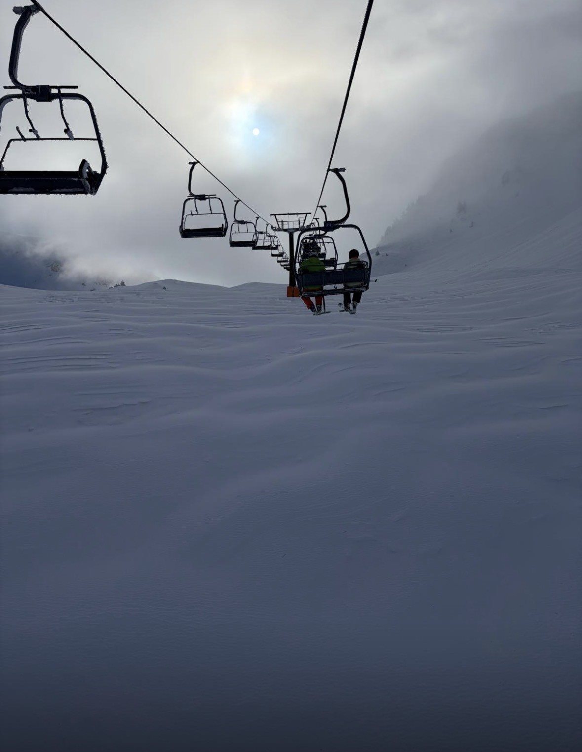 Two skiers riding a chairlift, silhouetted against the sky