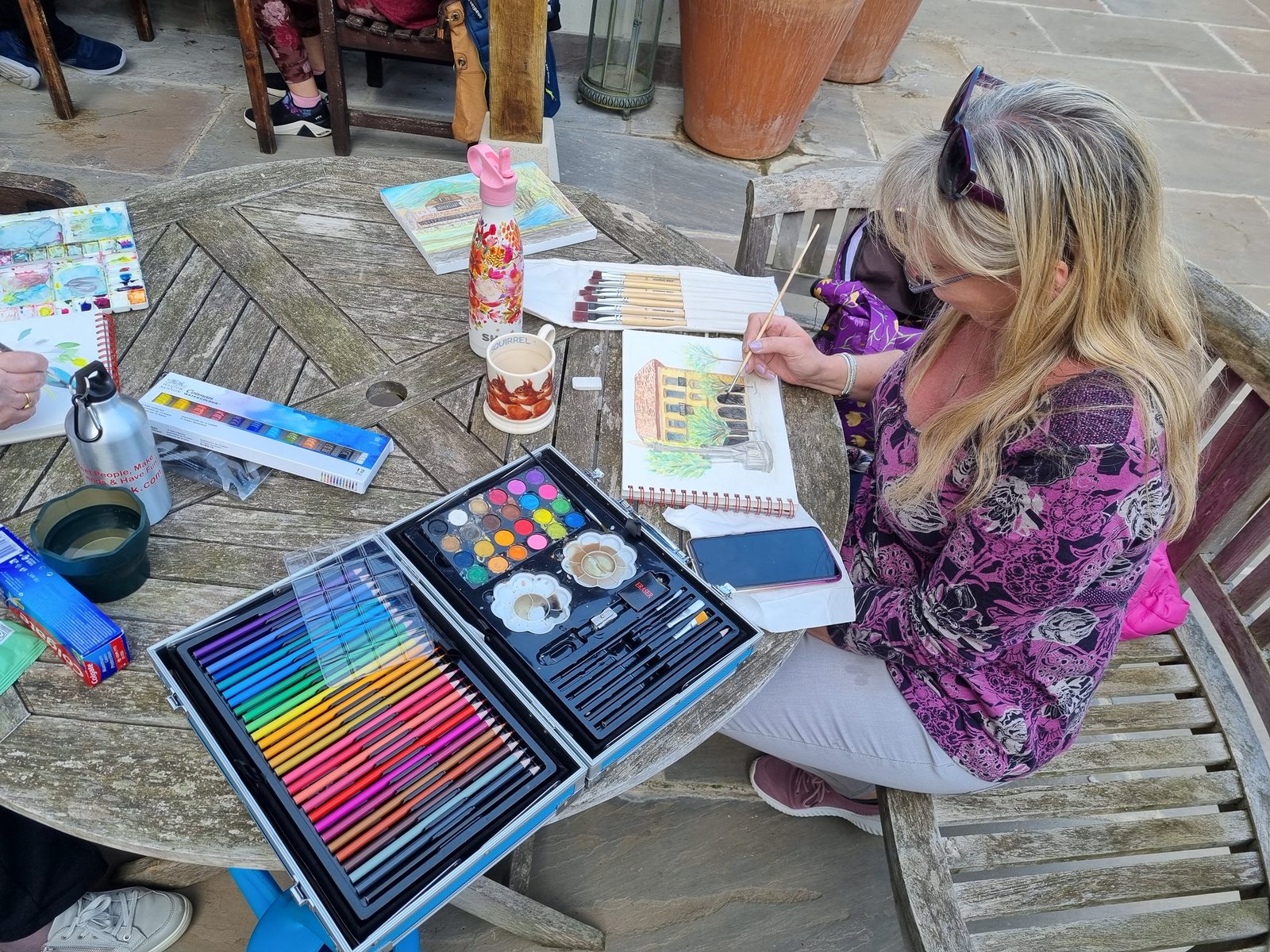 Woman painting outdoors at a table covered with art materials