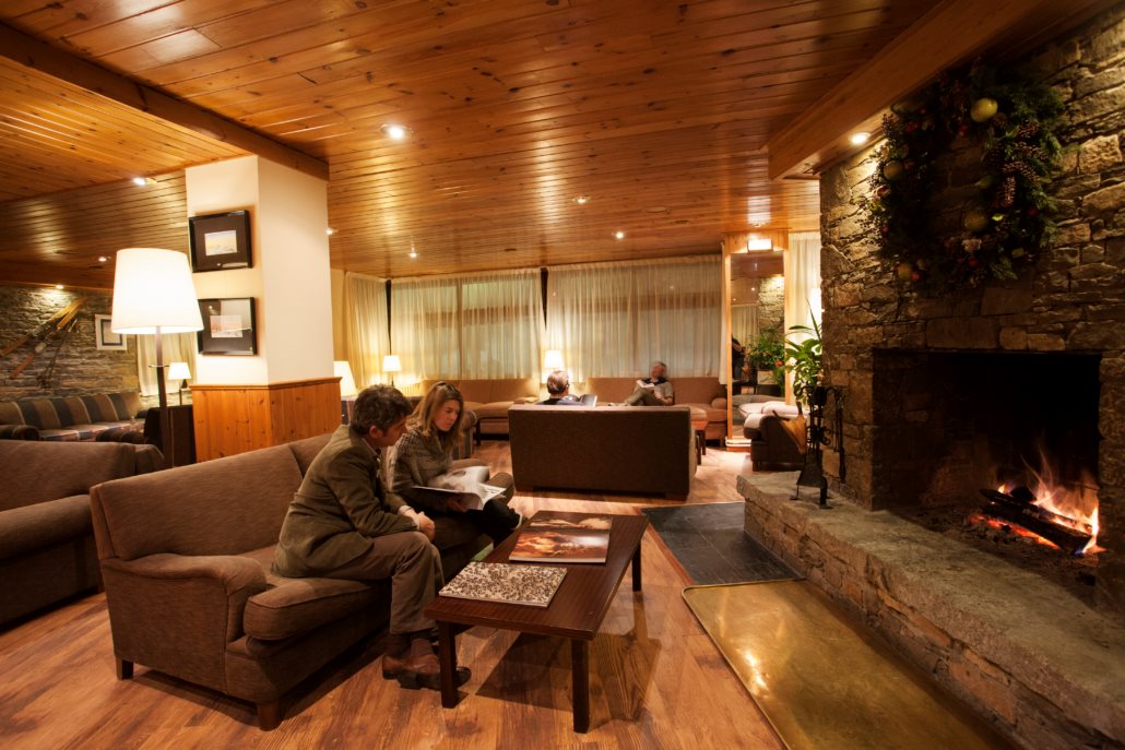 Guests relaxing by an open fire in a wood-panelled ski lodge lounge