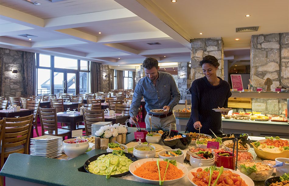 A man and woman serving themselves at a buffet spread of salads
