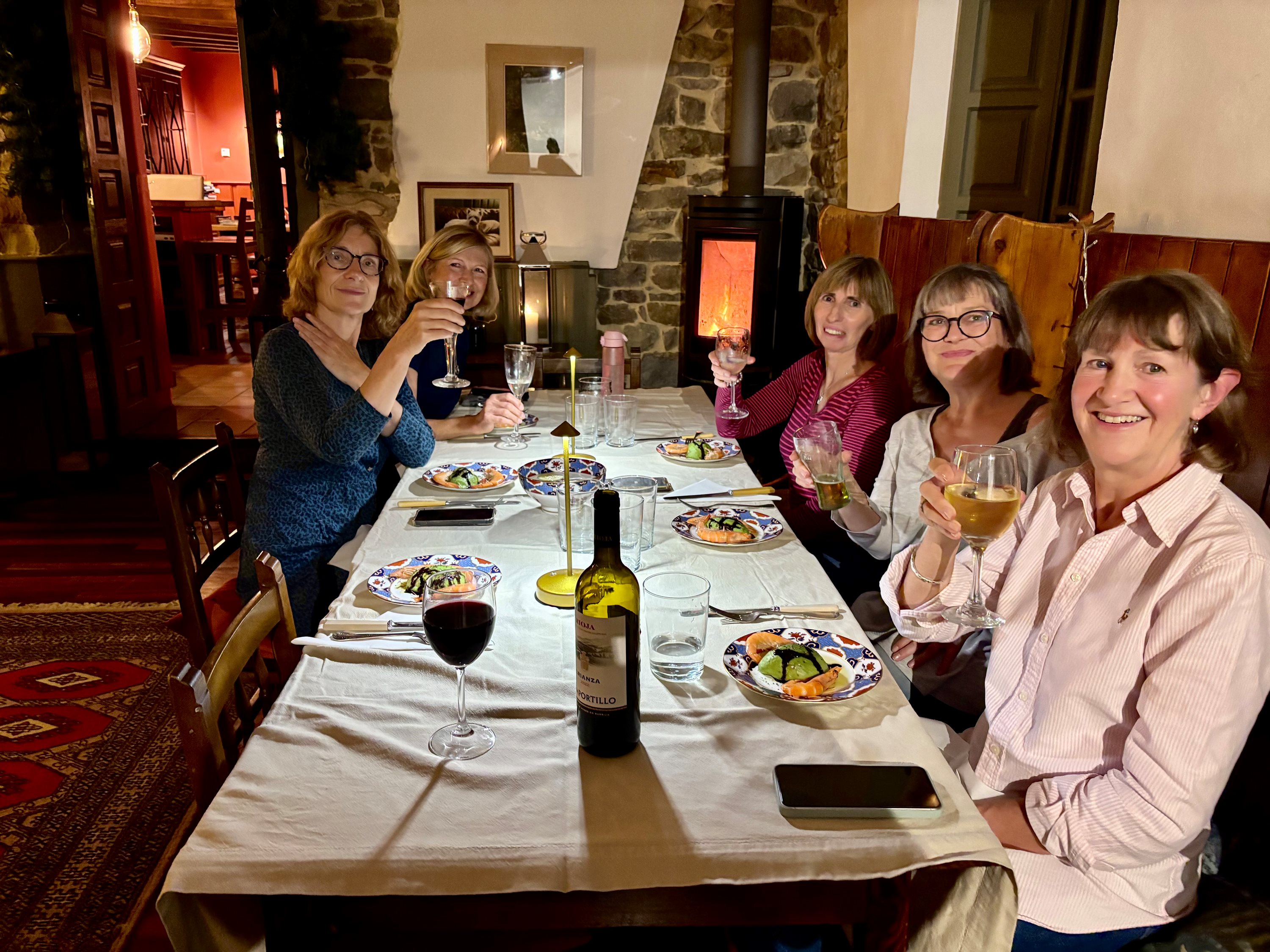 Five women raising wine glasses in a toast around a candlelit dinner table