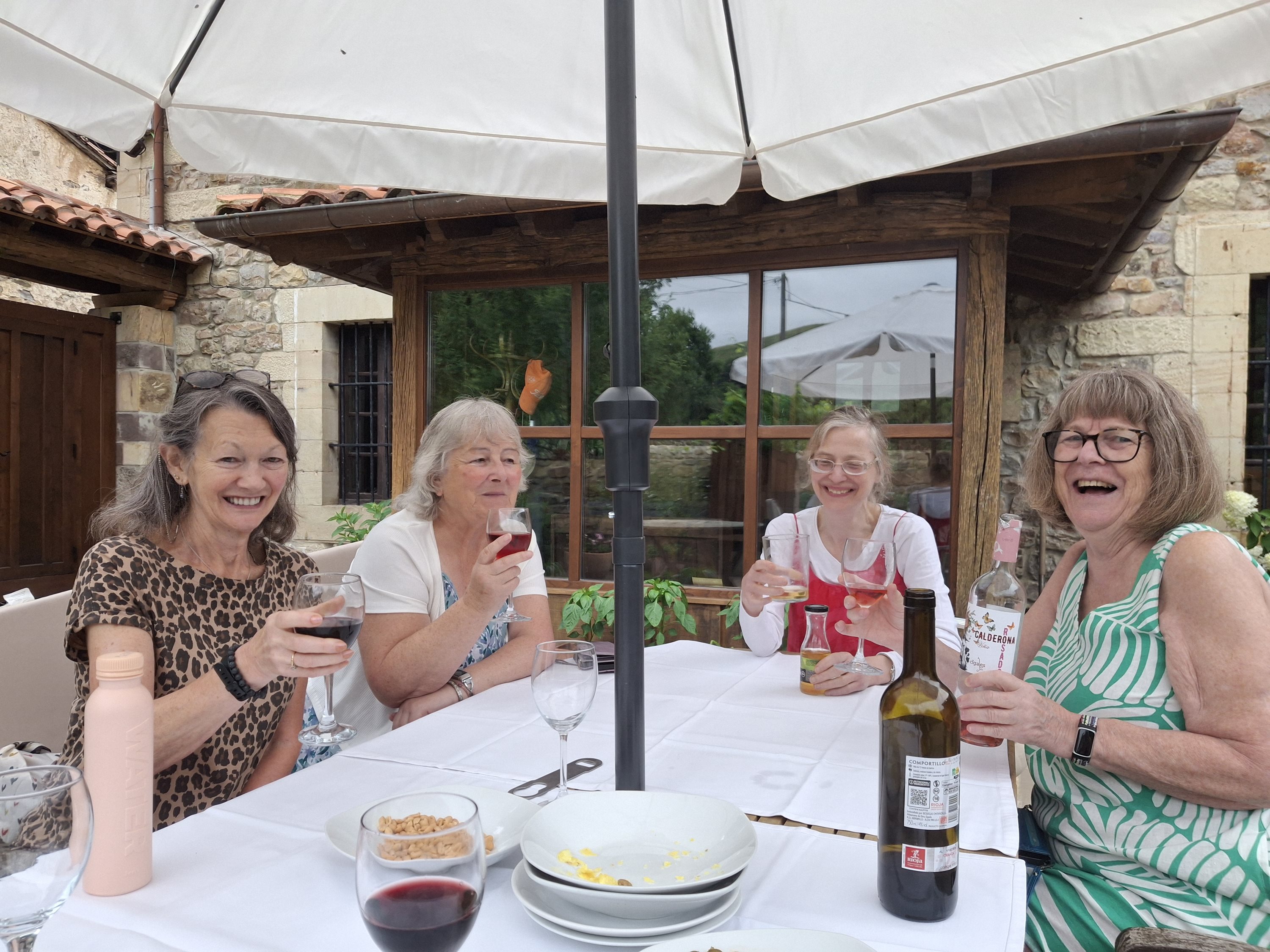Four women laughing and raising wine glasses at an outdoor table